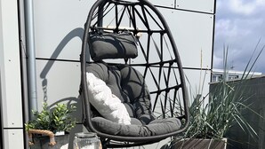 Una silla colgante con cojines, una mesita con una planta y un tapete tejido en una terraza en la azotea.