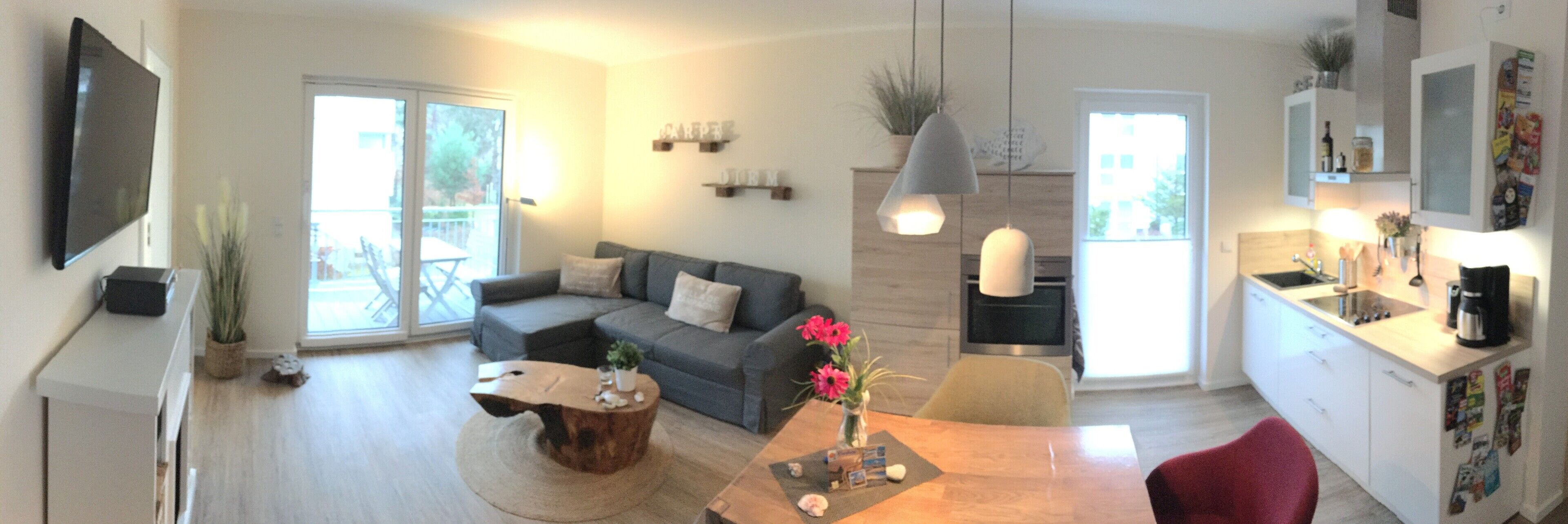 Ein modernes Wohnzimmer mit grauem Sofa, einem Holztisch und einem Esstisch mit Stühlen.