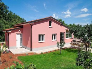 Une maison rose, de plain-pied, avec un petit jardin devant, une porte et des fenêtres.