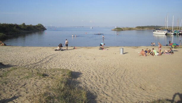 A sandy beach with boats docked in the water, people sunbathing, and a clear sky.