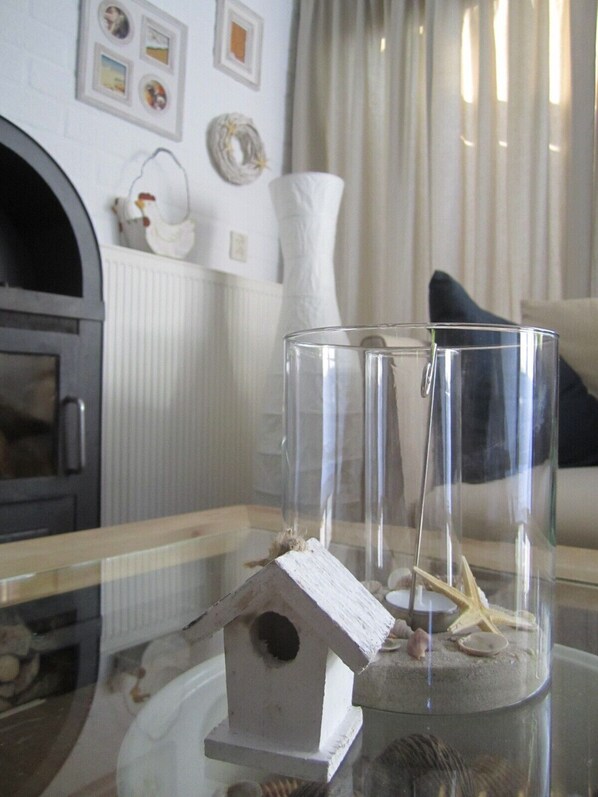 A clear glass birdhouse with a starfish and seashells inside, placed on a glass table.