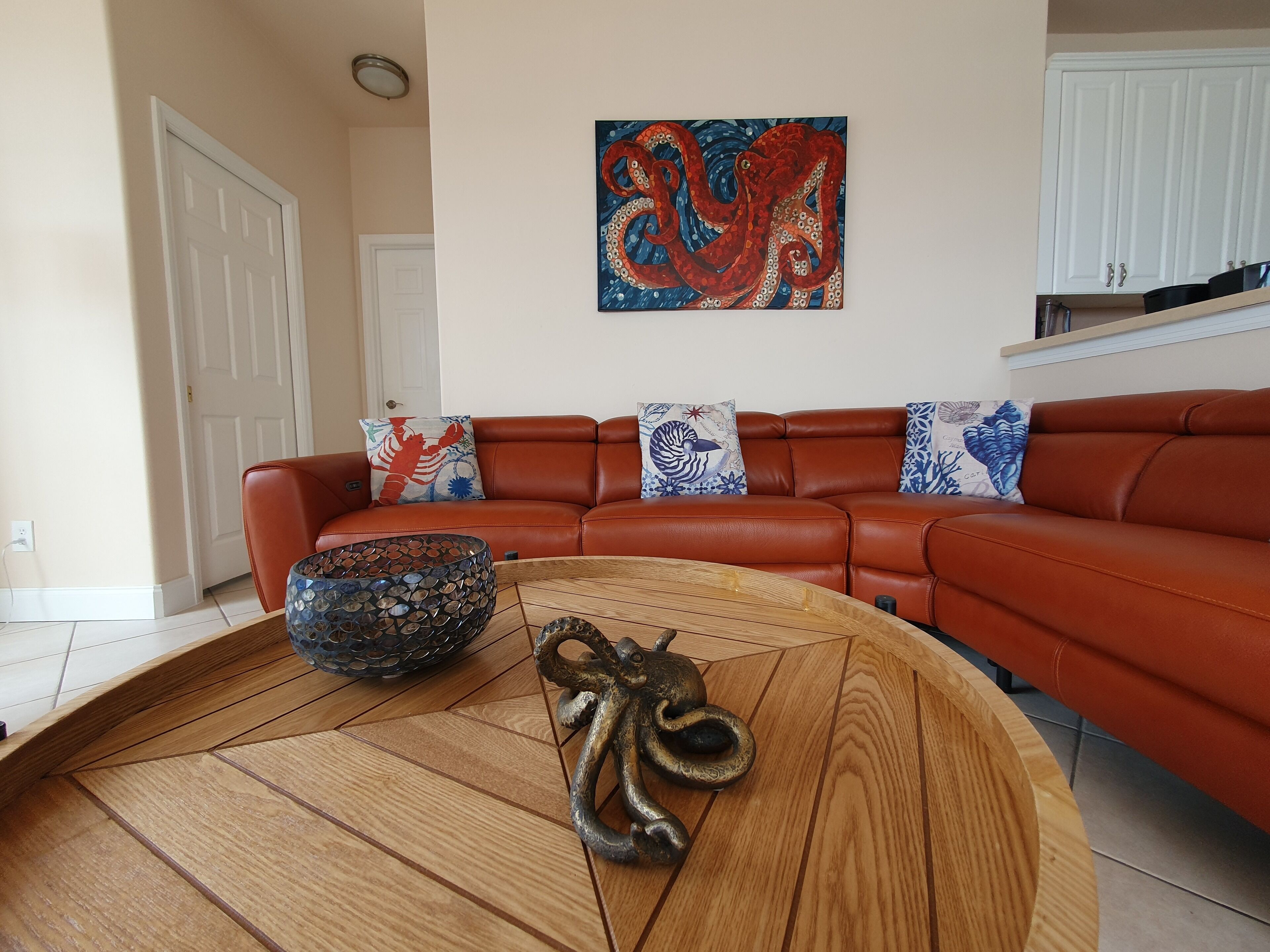 Een woonkamer met een bruine leren bank, decoratieve kussens, een houten salontafel en een kleurrijk octopus schilderij aan de muur.