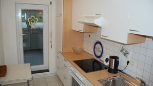 A compact kitchen with white cabinets, a sink, a stove, and a window with a decorative glass door. - Exclusive vacation apartment near the lake in a residential complex with a park-like garden (Überlingen)