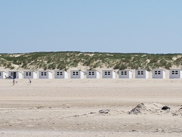 A row of beach huts with a sandy beach and dunes in the background.