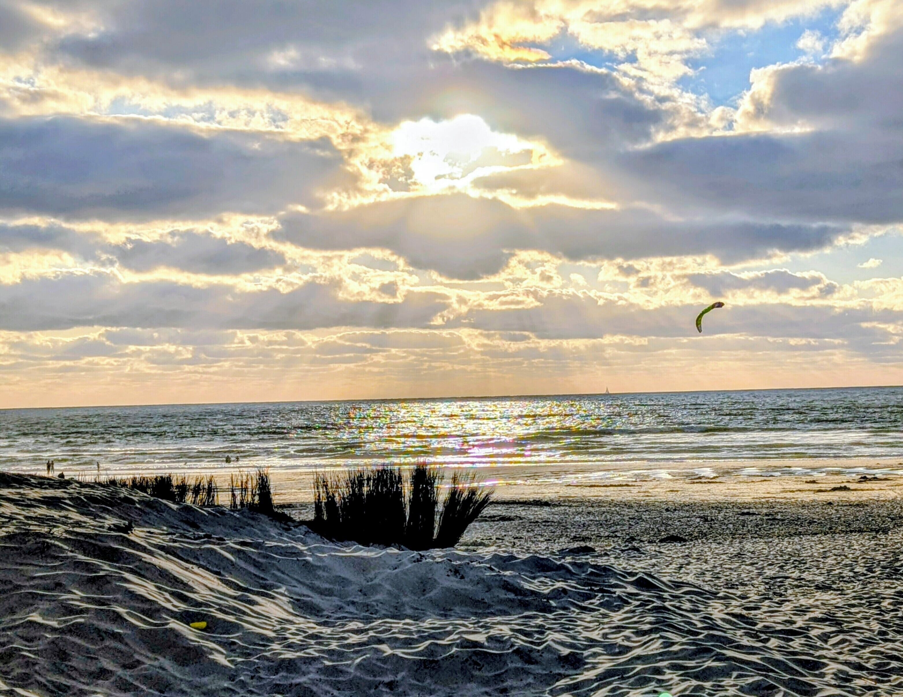 A beach with waves, a person flying a kite, and a sunset.