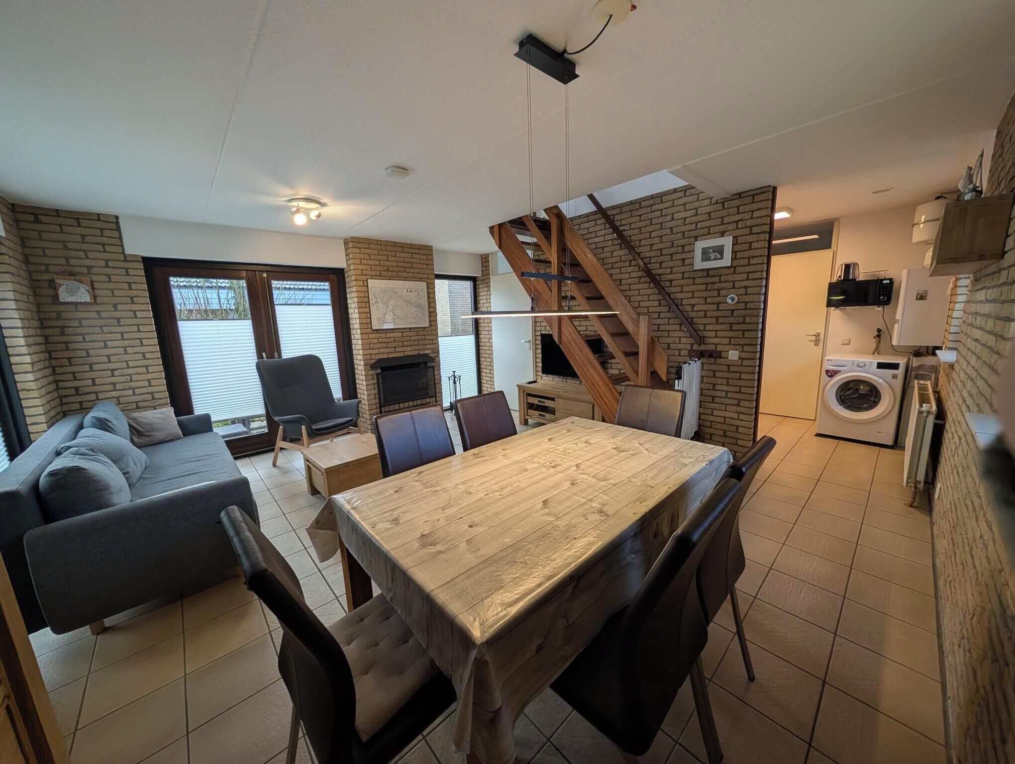 Een gezellige zithoek met een bank, een eettafel en een open haard. Een trap leidt naar een verdieping.