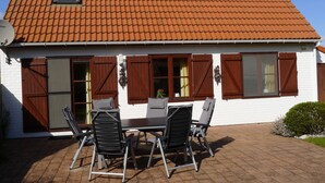 Une maison avec un toit recouvert de tuiles rouges, des murs extérieurs blancs et une terrasse avec une table et des chaises.