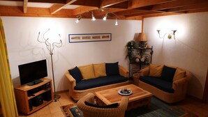 Un salon chaleureux avec deux canapés en osier, une table basse en bois, un téléviseur posé sur un meuble en bois et une lampe sur pied.