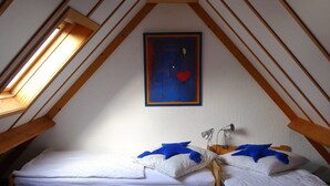 Une petite chambre mansardée, chaleureuse et accueillante, avec deux lits en bois, une lucarne et un tableau accroché au mur.
