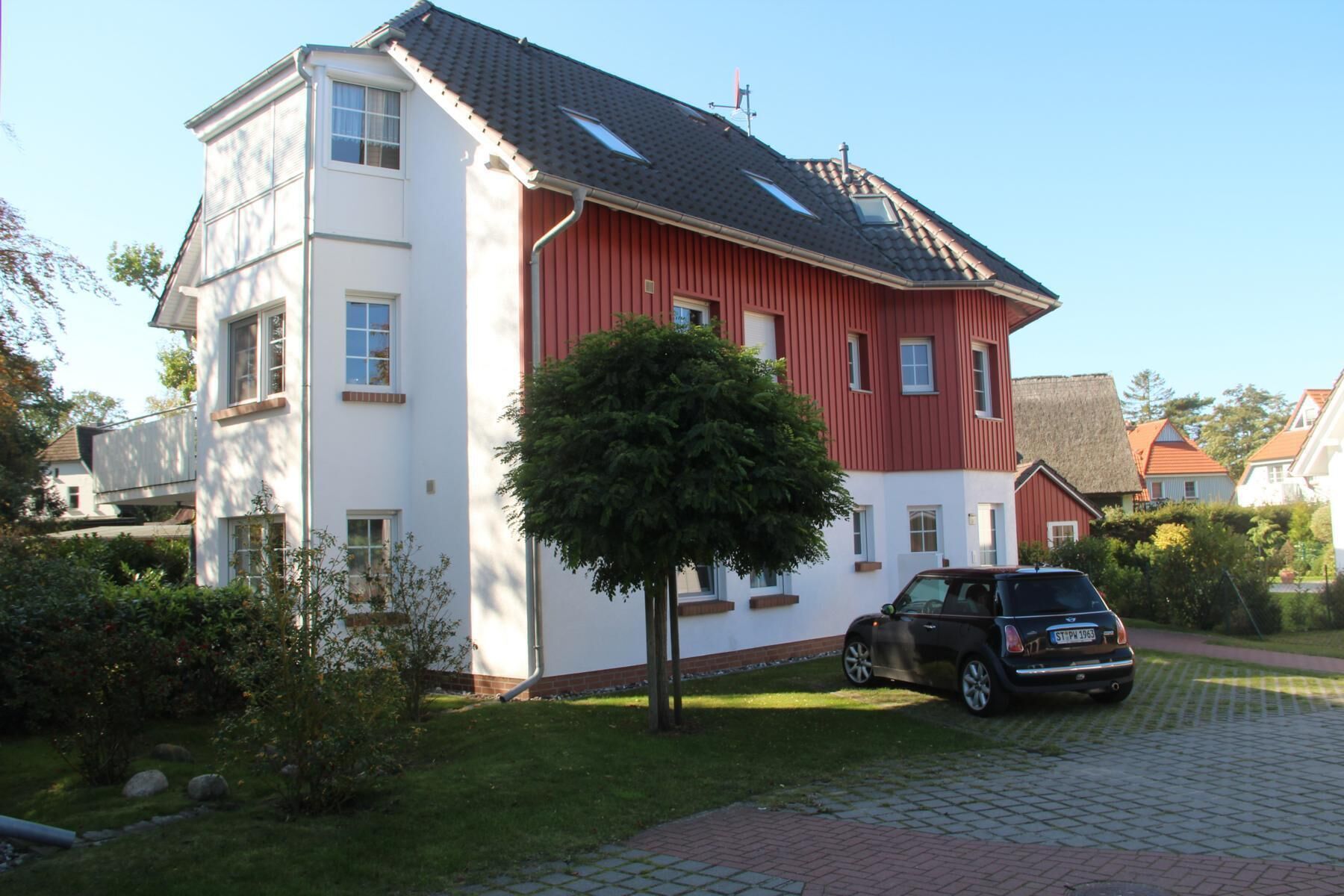 Een twee verdiepingen tellend huis met een rode en witte gevel, een oprit en een auto ervoor geparkeerd.