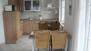 Una cucina compatta con mobili in legno, un forno a microonde, una macchina per il caffè e un'area pranzo con sedie in vimini.