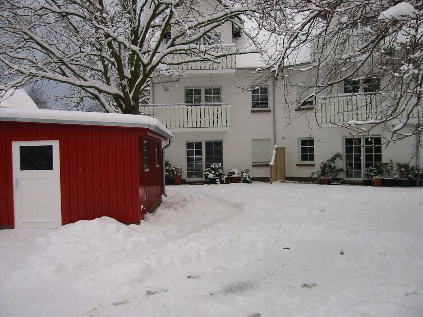 Un bâtiment à deux étages, à l’extérieur blanc, avec un abri de jardin rouge devant.