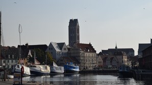 A historic town with a prominent clock tower, traditional buildings, and boats docked along the waterfront.