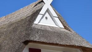 A house with a thatched roof, white walls, and red shutters.