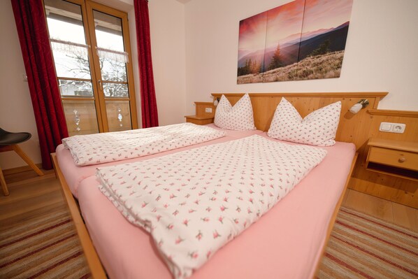 Un dormitorio con una cama grande, cabecera de madera, mesita de noche, una silla y una ventana con cortinas.