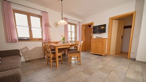 Un coin repas avec une table et des chaises en bois, un téléviseur fixé au mur et un espace cuisine doté de meubles en bois.