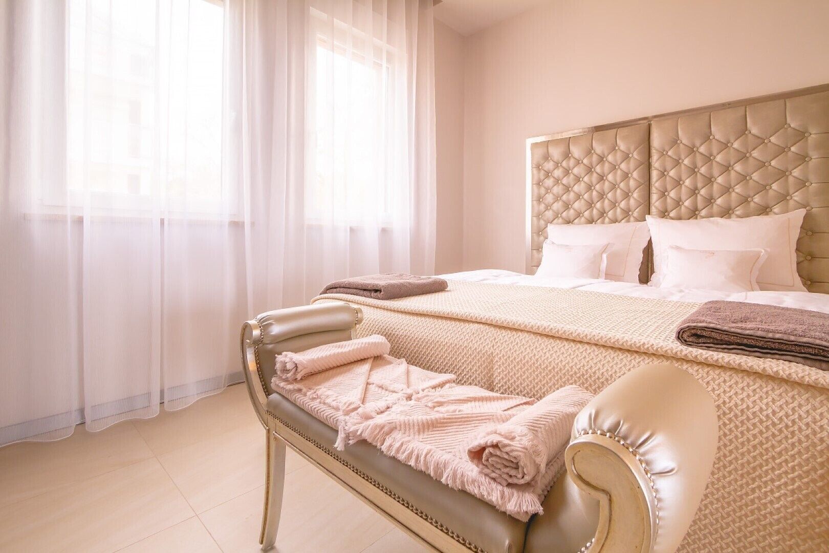 A hotel room with a large bed, a chaise lounge, and sheer curtains.