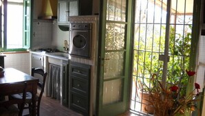 A kitchen with a stove, oven, and cabinets, a dining table with chairs, and a view through a glass door to a garden. - Splendio Rustico, nestled among olive and lemon trees, with a private pool. For Exclusive Use Only!! (Camaiore)