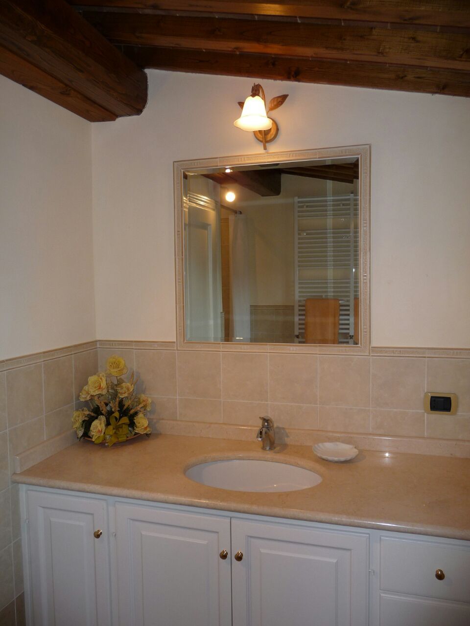 A bathroom with a sink, mirror, and wooden ceiling beams.