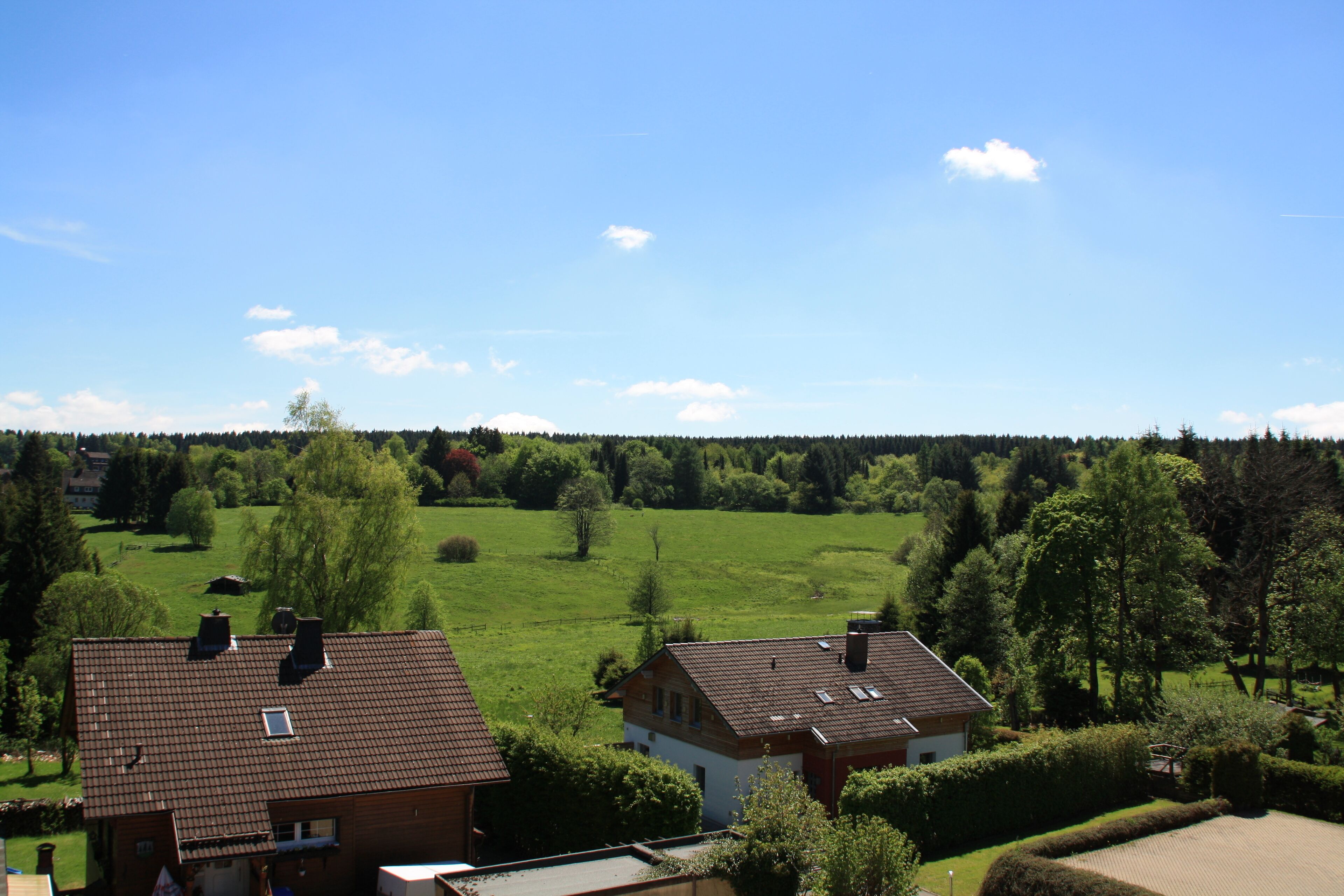 A residential area with two houses, one with a red roof and another with a brown roof, surrounded by green fields and trees.