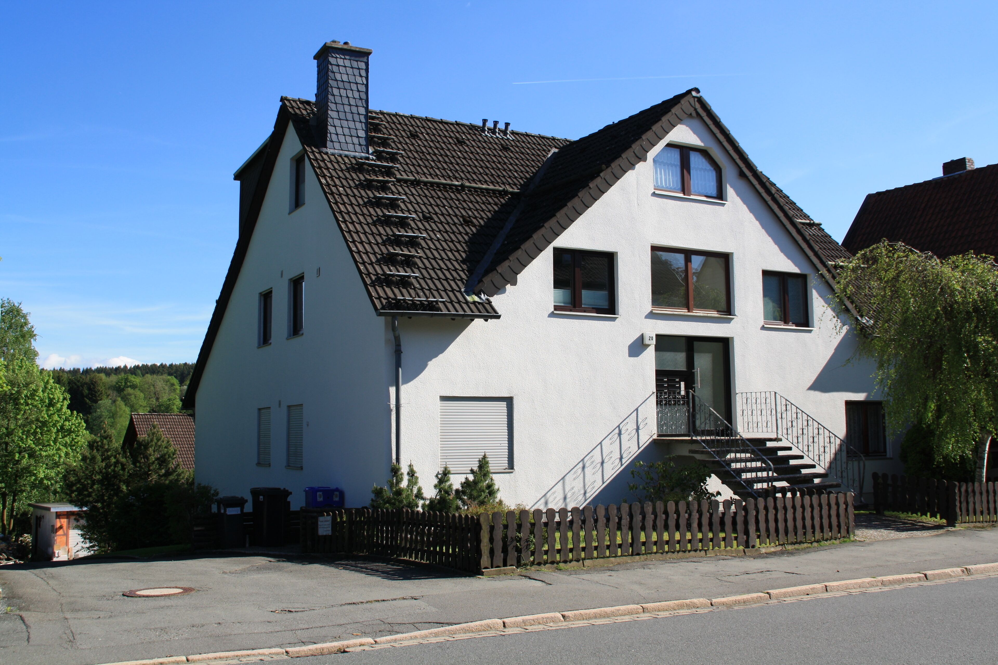 A two-story house with a sloped roof, a front porch, and a fenced yard.