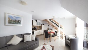 Een moderne woonkamer met een grijze bank, een eethoek met een rode tafel en een keuken op de achtergrond.