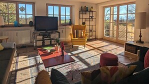A spacious living room with a large TV, a yellow armchair, and a bookshelf.
