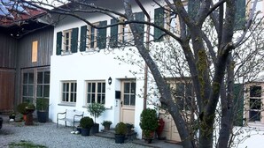 A white building with a door and windows, surrounded by potted plants and a gravel path.