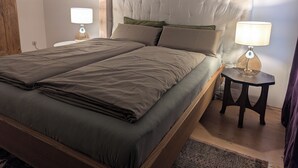 A double bed with a headboard, two bedside tables with lamps, a wooden floor, and a wall clock.
