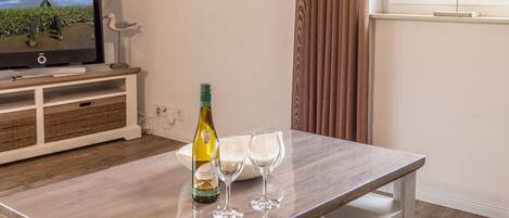 A wooden table with a bottle of wine and two glasses, a television, wicker baskets, and a clock on the wall.