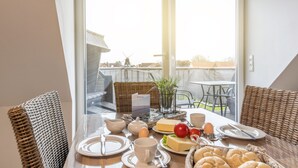 Een ontbijtarrangement met een tafel, rieten stoelen en een uitzicht op een windmolen door een glazen deur.