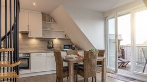 Een moderne keuken met witte kasten, een houten eettafel, rieten stoelen en uitzicht buiten door grote schuifdeuren.