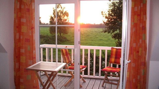 A balcony with a table and two chairs, a view of a green field, and a sunset. - North Friesland - In the Land of Horizons (Seeth)