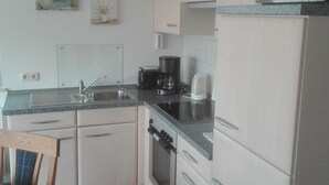 A compact kitchen with white cabinets, a built-in oven, a microwave, and a coffee maker. - North Friesland - In the Land of Horizons (Seeth)