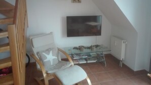 A room with a wooden chair, a glass table, a wall-mounted TV, and a radiator. - North Friesland - In the Land of Horizons (Seeth)