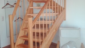 A wooden staircase with a handrail, a chair with a starfish pillow, and a wall-mounted coat rack with hangers. - North Friesland - In the Land of Horizons (Seeth)