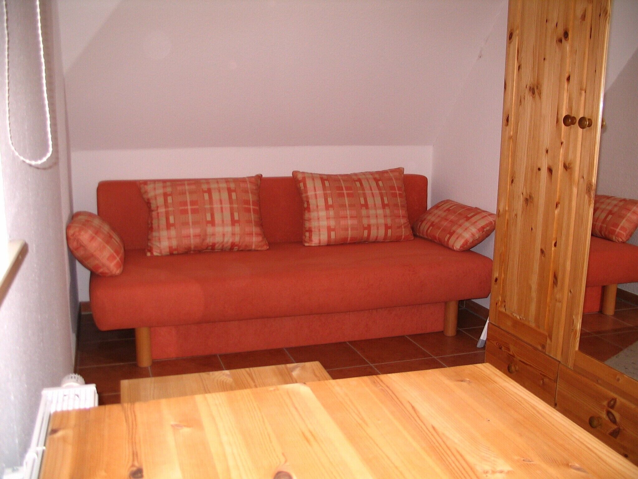 Een rode bank met geruite kussens, een houten tafel en een houten garderobe met spiegel.