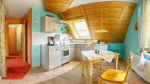 Eine kompakte Küche mit Holzbalkendecke, einem Essbereich mit Tisch und Stühlen sowie einem kleinen Fenster, das für natürliches Licht sorgt.