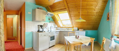 A compact kitchen with a wooden ceiling, a dining area with a table and chairs, and a small window providing natural light.