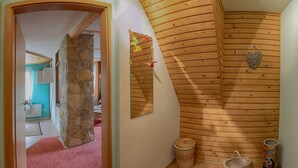 Ein Zimmer mit Steinwand, Holzboden und rotem Teppich. Auf dem Boden steht ein Korb und ein dekorativer Gegenstand.