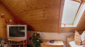 Ein gemütliches Schlafzimmer im Dachgeschoss mit geneigter Holzbalkendecke, einem Fernseher, einem kleinen Tisch und einem Bett mit blumigem Bettzeug.