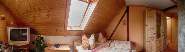 A cozy attic bedroom with a sloped wooden ceiling, a television, a small table, and a bed with floral bedding.