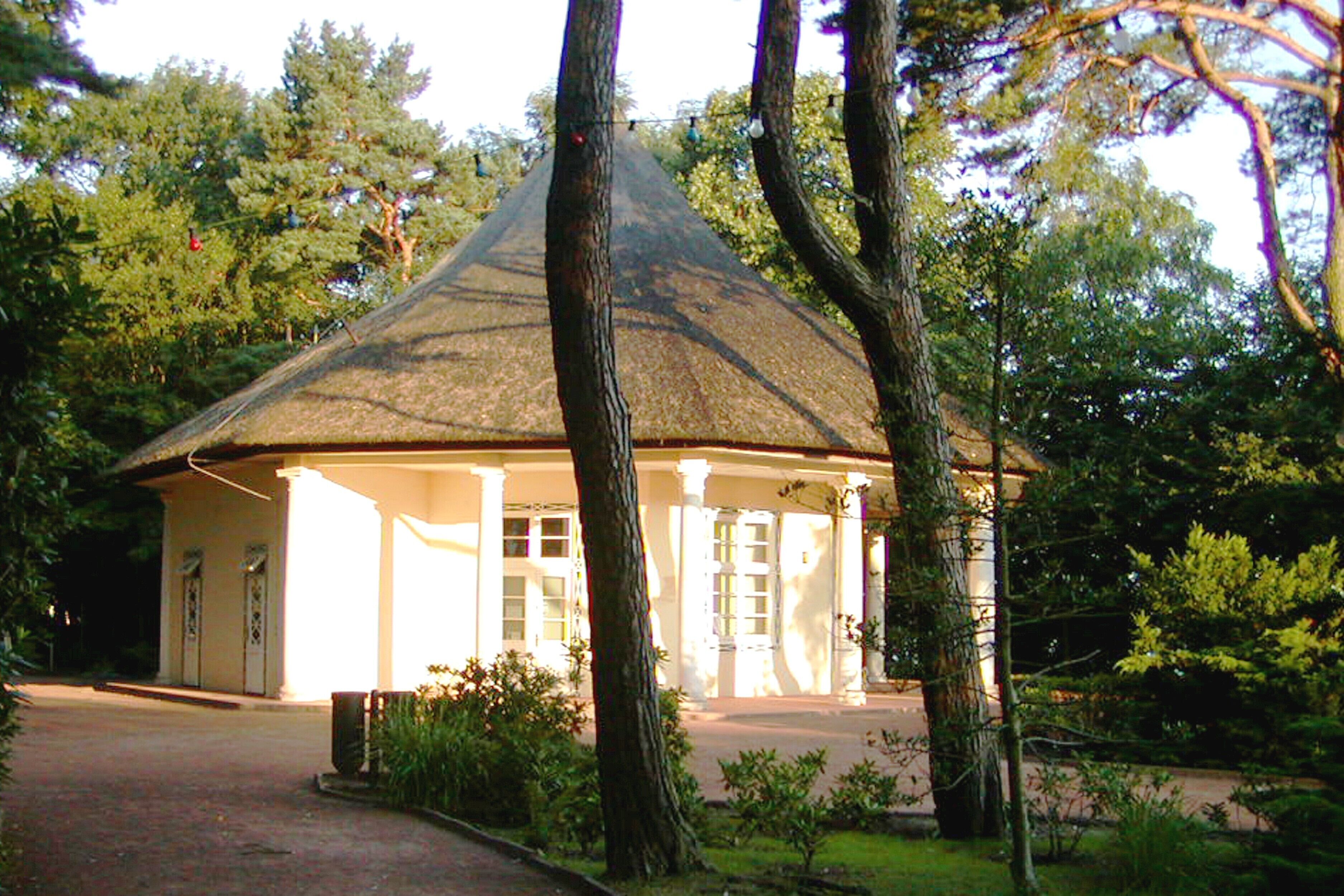 A building with a conical roof, surrounded by trees and a pathway leading to the entrance.