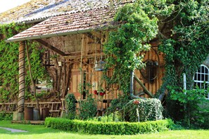 Un edificio de madera rústico con techo de tejas, rodeado de abundante vegetación y un jardín cuidado.