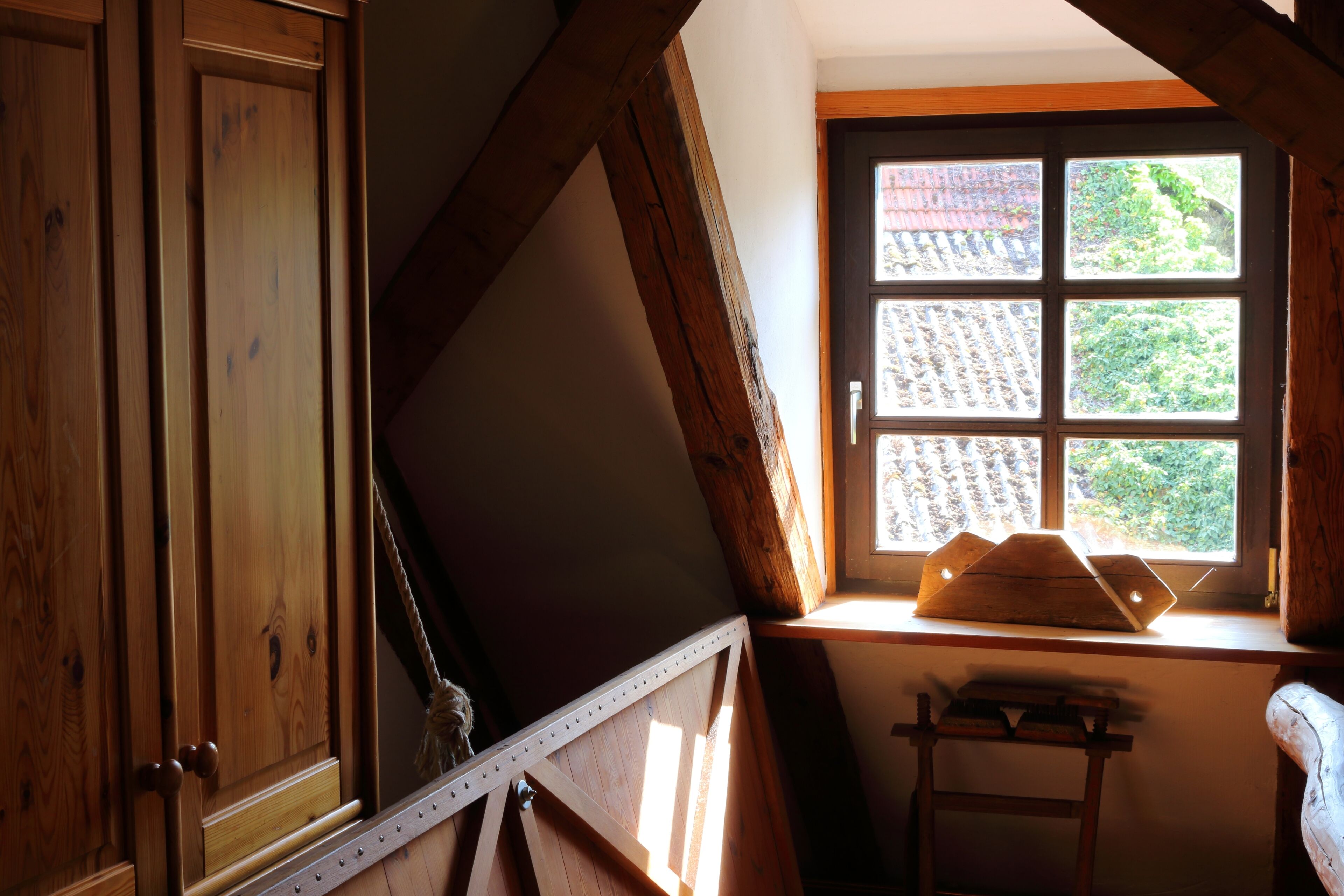 Ein Zimmer mit Holzbalken, einem Fenster mit Blick auf Grünflächen und einem Holztisch.