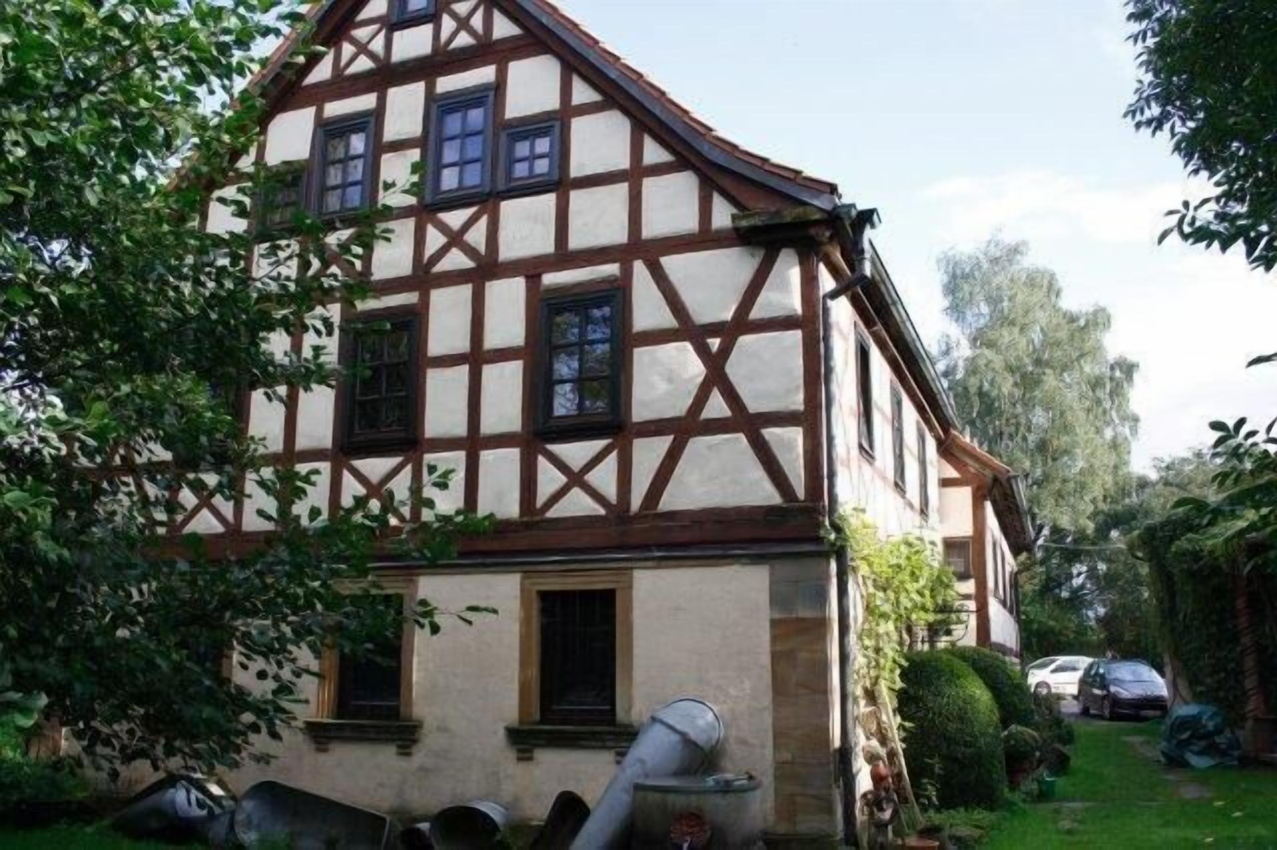 A traditional half-timbered house with a sloped roof, a small front porch, and a visible chimney.
