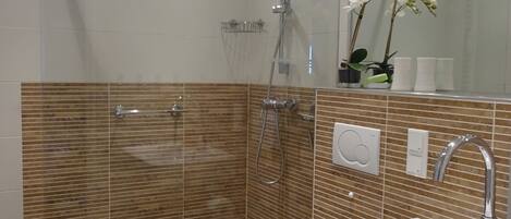 Un baño moderno con ducha de vidrio, un lavamanos blanco y un espejo sobre él.