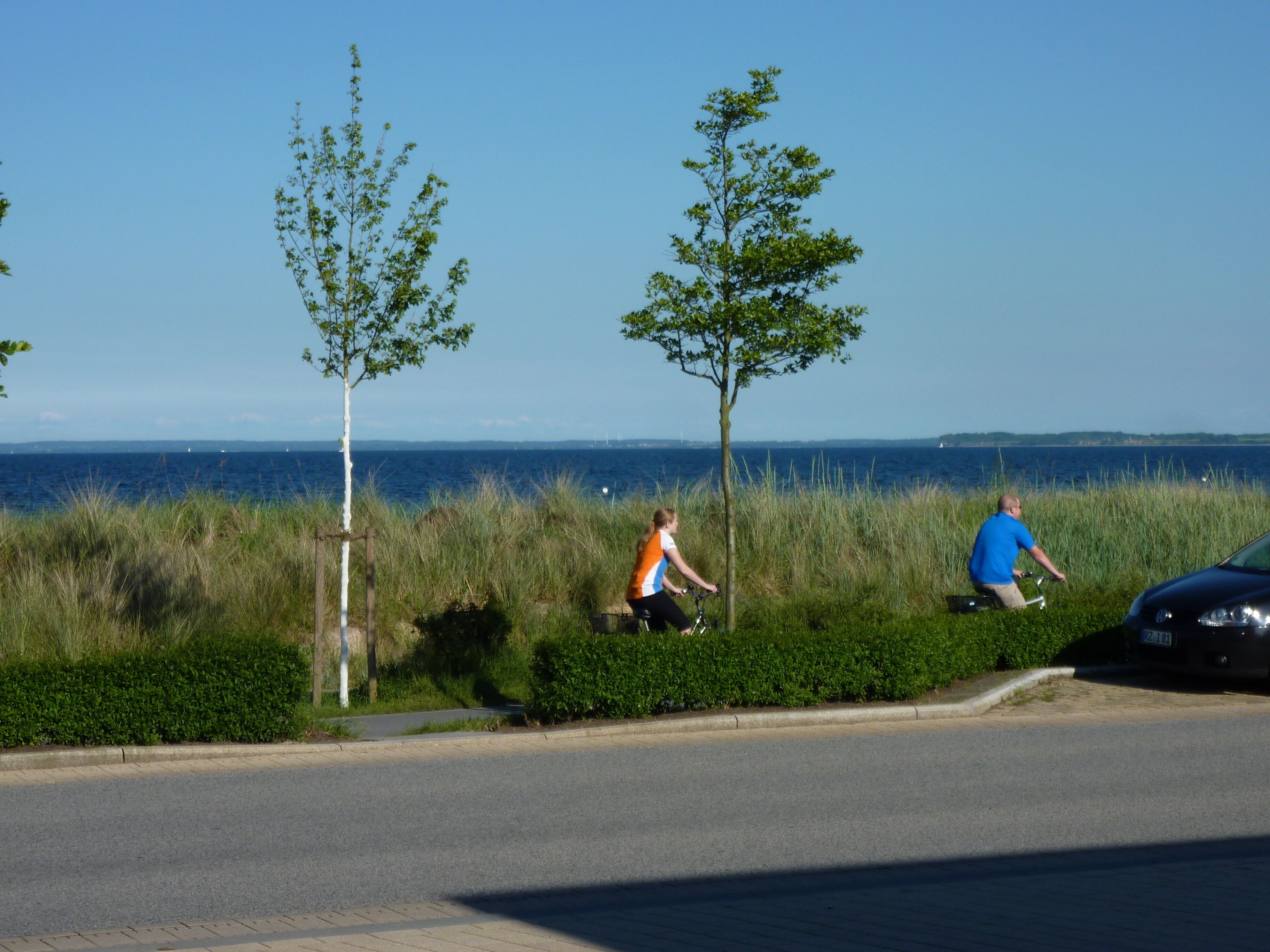 A coastal road with two cyclists and a parked car.