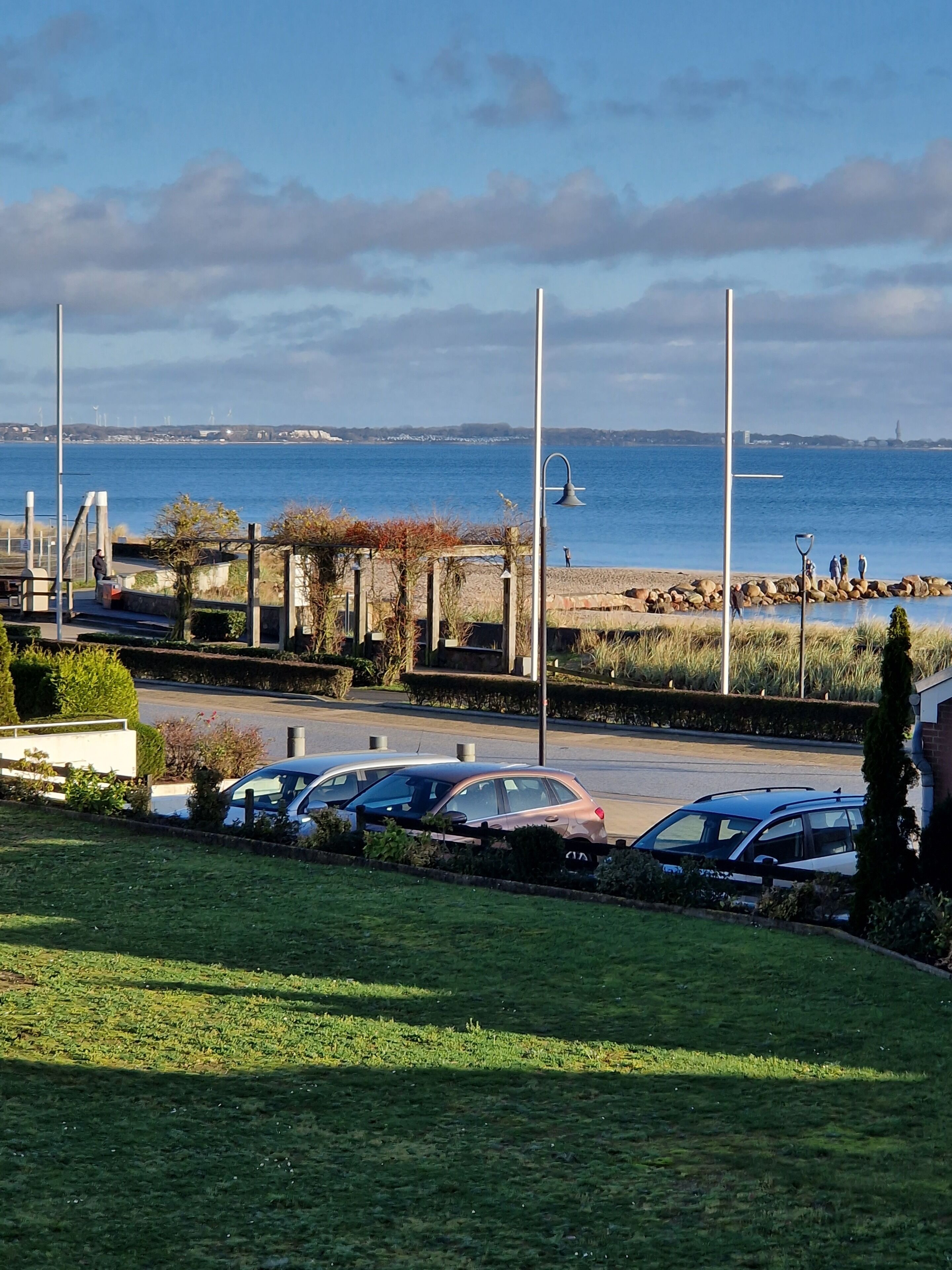A parking area with cars, a grassy field, and a view of the sea.