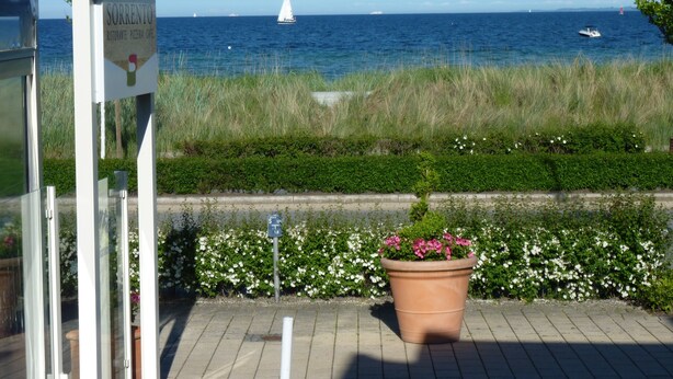 Schild für 'Sorrento Restaurant, Pizzeria, Cafe' mit Blick auf das Meer und Boote.